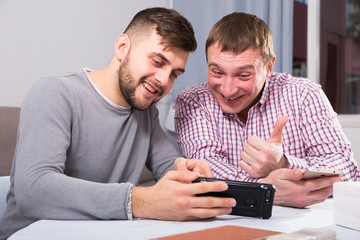 Canvas Print - Happy male friends using phone at home table