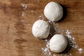 Wall Mural - Dough for pizza cooking. Three balls of fresh homemade wheat dough on wooden table. Home baking. Flat lay, space