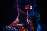Fototapeta Psy - ethnic fluorescence patterns on cropped young woman's body, skin. creative body art, in neon lights. unusual shoot of woman showing silence gesture