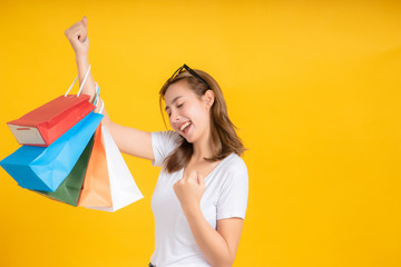 Happy young asian woman with shopping paper bag fashion purchase on store shopping mall concept in white t-shirt smiling emotion on yellow background isolated studio with copy space.