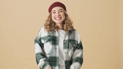 Sticker - Happy pretty woman in knit hat and shirt rejoicing and holding hands together over beige background