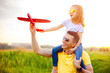 © zamuruev - Cheerful man smiling and carrying excited girl on shoulders while playing with red aircraft together against cloudy sky on sunny summer day
