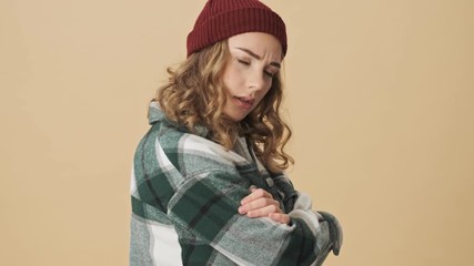 Poster - Upset pretty woman in knit hat and shirt standing with crossed arms and looking at the camera over beige background