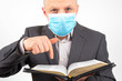 man in a business suit with a medical mask on his face is studying the bible.