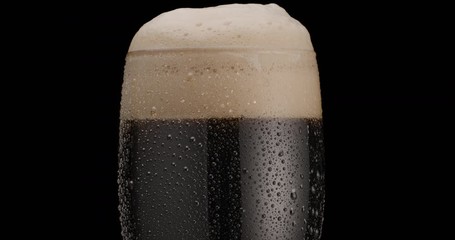 Canvas Print - Glass of black beer on a black background. Beer sways in the glass, bubbles and foam rise. Glass of beer rotates slowly clockwise.