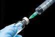 © arcyto - Doctor's hand holding medicine bottle and syringe isolated on black background.Nurse using syringe are vaccination to patient for influenza protection.Coronavirus vaccine against concept.