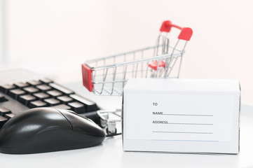 Red trolley, computer mouse and laptop keyboard.A cart and box product for send to customer on wood table.Electronic commerce that allows consumers to directly buy.Shopping online concept.