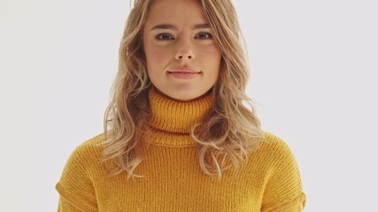 Wall Mural - Pretty blonde woman in sweater looking at the camera and becoming happy over grey background