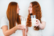 © studioprodakshn - glasses with milk held by two redheaded young women on isolated white backgroung, healthy dieting concept