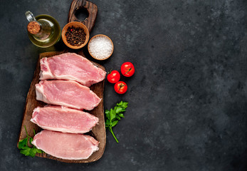 raw pork steaks with spices on a cutting board on a stone background