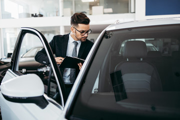 Poster - Car seller working in showroom and quality control checking of car details for the last time before buyer comes.