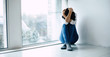 © My Ocean studio - Isolation. Photo of an adult woman who is sitting near the window and hugging her head with her hands crossed while crying and suffering from self-isolation.