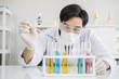 © mrwinn - A male scientist with black hair wearing white coat and protective glassware and face mask dropping liquid solution from a pipet into a test tube looking serious in a laboratory setting.