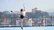 © Artem - Elegant dancer. Beautiful slim sports model. Beautiful girl with long legs performs a dance pose balancing on one leg and toes. Woman on a cruise ship against the background of the Asian port city