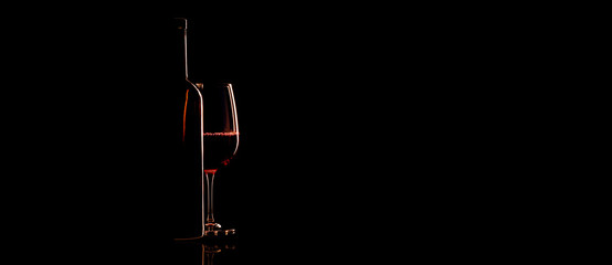 Elegant red wine glass and a wine bottle over black background