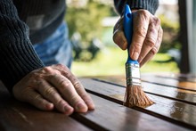 Senior Man Painting Wooden Table. Renovation Of Garden Furniture. Close Up Hand With Paintbrush