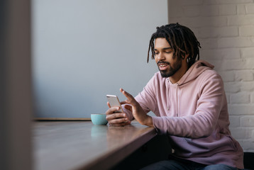Happy African American man with stylish dreadlocks holding mobile phone, communication, shopping online. Young smiling freelancer using modern technologies, working from home