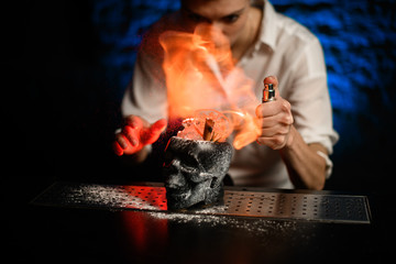 Bartender sprays and makes fire over glass in form of black skull with ice