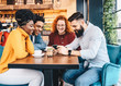 © Sanja - Four friends looking at the phone in a cafe.
