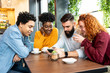 © Sanja - Four friends discussing a topic while looking at the phone in the cafe.