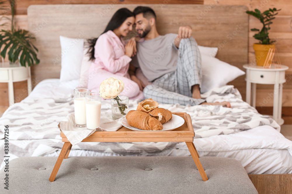 Young couple with breakfast resting on bed at home