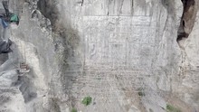 Aerial Sliding Shot Of Buddhist Sculptures Carved Into The Rock Face Of The Hill, The Giant Buddha Statue With Bamboo Scaffolding In Construction
