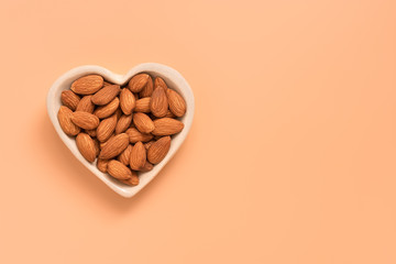 Almond nut in a heart shape bowl on a pastel pink background. Healthy eating concept. Top view, flat lay, copy space.