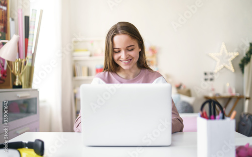 Cuadros en Lienzo Young female student sitting at the table, using laptop in quarantine