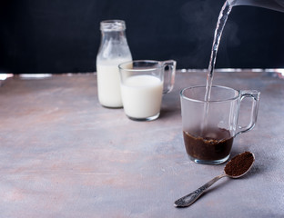 Wall Mural - Brewing coffee in a glass cup, a jet of hot water, milk in a bottle, a spoon with custard coffee on the table