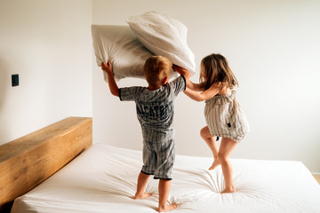 two kids at home having a good time playing pillow fight on parents bed on morning daylight