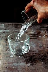 Wall Mural - Hand pouring water from a glass into a transparent cup with a splash and splashes on a black background