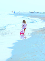 Rest and travel. Beautiful  little Caucasian girl on the sea blue coast  in a dress light pale pink with a children's pink suitcase for holidays goes on the move and enjoys