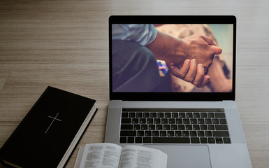 Worship from home, Online live church for sunday service, Laptop screen with close up prayer hands, Bible on wooden table, quarantine for Covid 19 situation