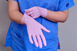 © Андрей Журавлев - The doctor puts on pink protective gloves, close-up. Hands of a medic in a blue uniform.