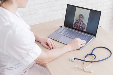 gp hosts an online appointment with an elderly quarantined patient at home. Female doctor at the desk talking to an elderly woman on a web camera and gives treatment recommendations