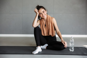 Canvas Print - Photo of joyful brunette woman smiling while sitting on mat