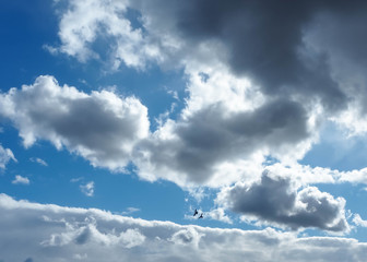 Blue sky with gray fragments, rays of the sun and two dark silhouettes of a bird in the distance. Background