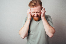Closeup Portrait Of A Young Hipster Red Bearded Man In Shirt Holding Hands To Ears Covering To Shut Out Noise Looking  At Neighbors