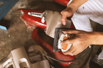 closeup mechanic worker sanding polishing motorcycle body and preparing for painting at station service with soft-focus and over light in the background