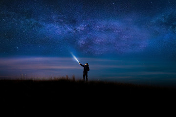 Night sky with  Milky Way and silhouette of a standing happy man with classic blue light. Image soft focus and noise due to long expose and high iso.