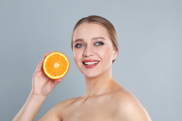 Sticker - Young woman with cut orange on grey background. Vitamin rich food