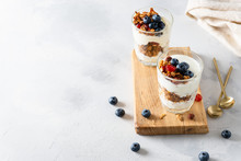 Healthy Breakfast. Muesli With Blueberries, Almonds, Raisins, Hazelnuts, Honey And Yogurt In Glasses On A White Concrete Background. Side View, Copy Space. Recipe
