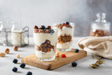 Wall Mural - Healthy breakfast granola, muesli with blueberries, nuts, honey and yogurt in glasses on gray concrete background. Side view