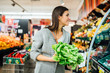 © eldarnurkovic - Young woman shopping in the supermarket grocery store for fresh greens.Buying organic vegetables sustainable produce.Natural source of vitamins and minerals.Vegan/vegetarian diet.Nutritional value