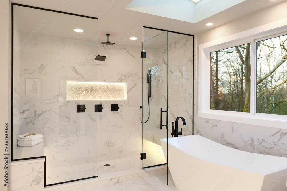 Detailes of the larhe walk in shower with white marble and mosaic, light. Three handles, shower head in dark brass.and free standing modern tub. - obrazy, fototapety, plakaty 