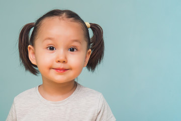 Pretty little girl standing on a blue background with ponytails.