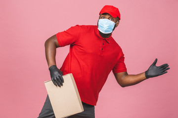 Delivery african american man employee in red cap blank t-shirt uniform face mask gloves hold empty cardboard box isolated on pink background. Service quarantine pandemic coronavirus virus 2019-ncov.