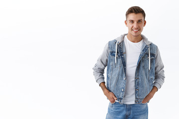 Handsome caucasian blond guy with blue eyes, hold hands in pockets and smiling pleased, looking camera with enthusiastic satisfied expression, standing white background joyful