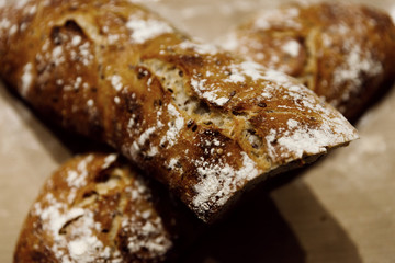 two baked homemade bread lie on the table,homemade baked bread with seeds,baguette sprinkled with flour,fresh bread on a black background,fresh bread texture