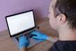 © Катерина Бухвалова - A man sits with laptop and uses blue gloves. Pandemic coronavirus 2020. Quarantine. Virus concept. Epidemic infection.